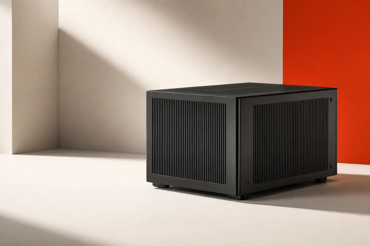Concept render of an Atarla Node: a matte black enclosure with fine ventilation slots, on a pale surface beside an orange wall.